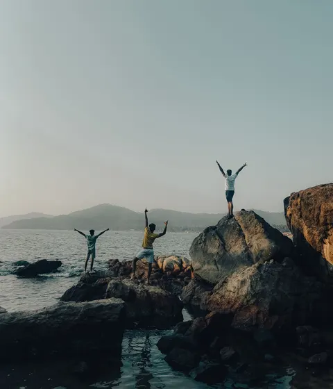 Three friends standing on the rocky coast in Goa